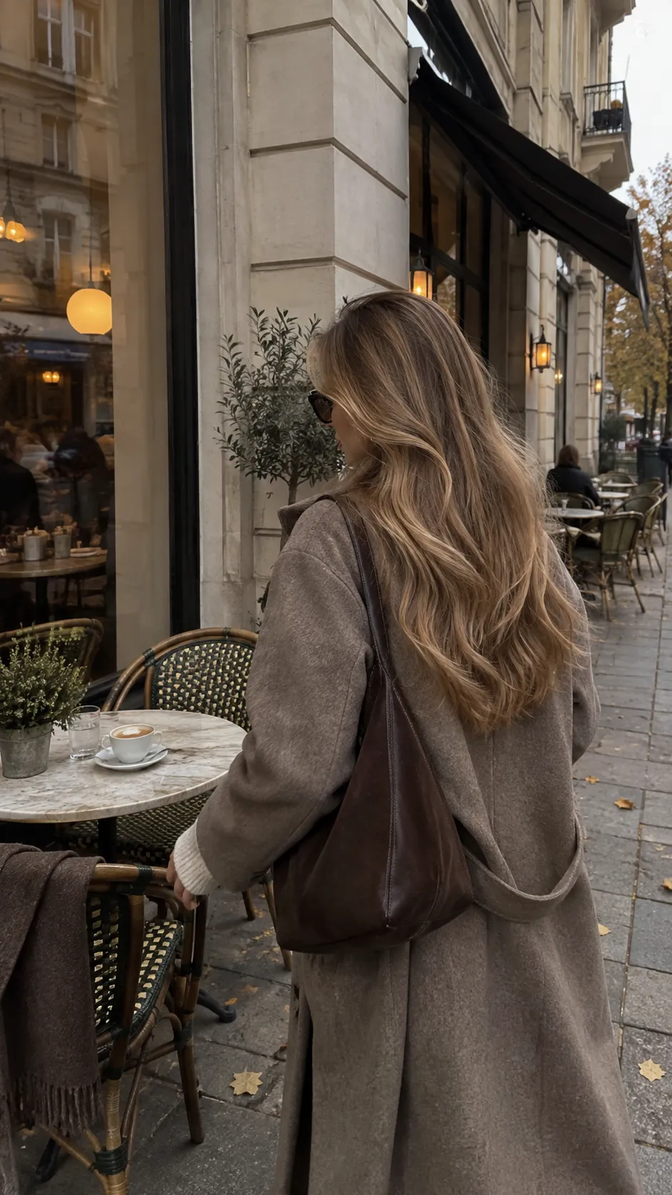 Kvinne i beige kåpe med skinnveske utenfor en kafé